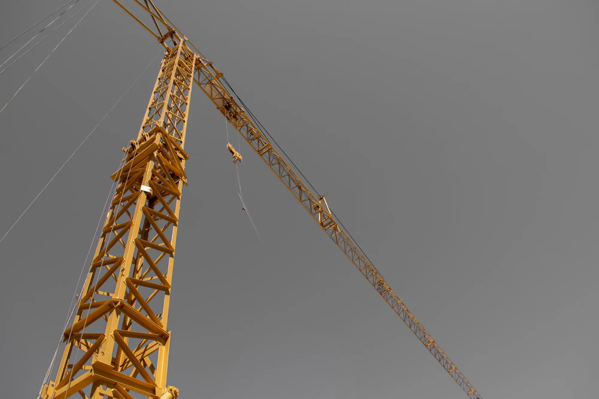 A yellow tower crane seen from below against a flat grey sky